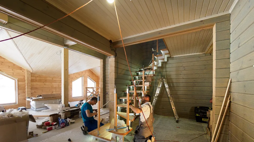 Artisans réalisant des travaux de rénovation intérieure dans une maison, avec installation d’un escalier et aménagement en bois.
