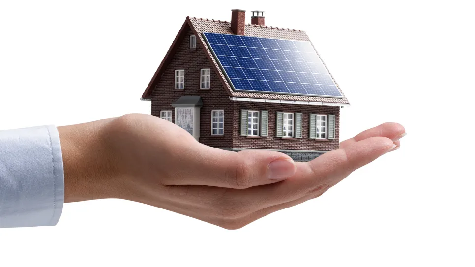 Maison avec panneaux solaires tenue dans une main – solution d’énergie renouvelable pour habitation.